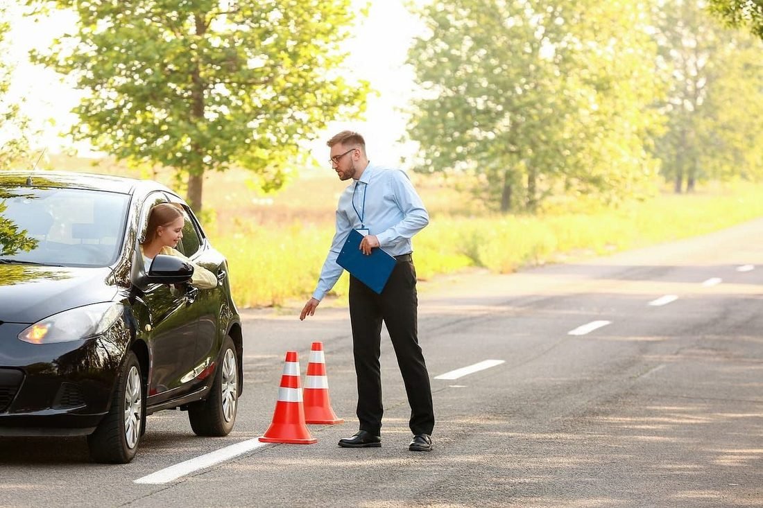 Un moniteur d'auto-école donne des consignes à une élève au volant, près de deux plots sur la route